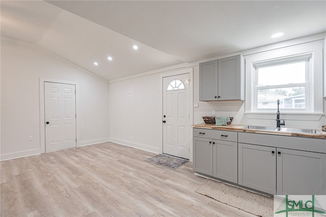 kitchen with gray cabinetry, light wood-type flooring, lofted ceiling, and sink