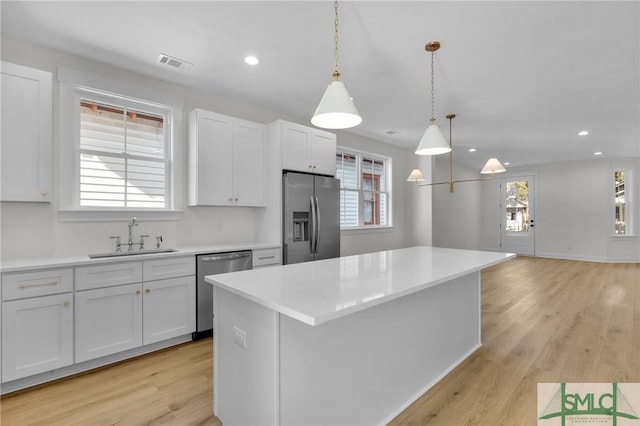 kitchen featuring appliances with stainless steel finishes, sink, decorative light fixtures, white cabinets, and a kitchen island