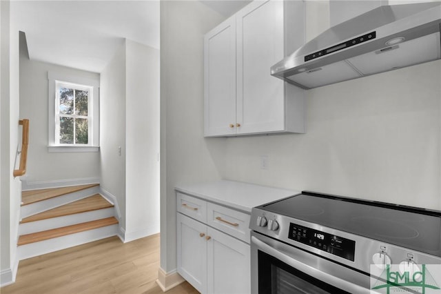 kitchen with white cabinets, stove, and wall chimney exhaust hood