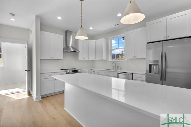 kitchen with white cabinetry, wall chimney range hood, stainless steel appliances, and hanging light fixtures