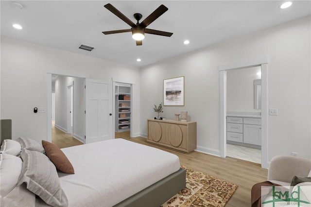 bedroom with light wood-type flooring, a walk in closet, ensuite bath, ceiling fan, and a closet