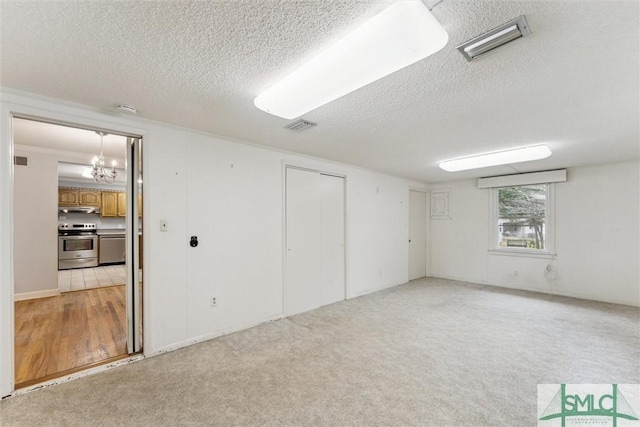 unfurnished room featuring light carpet, a textured ceiling, and a notable chandelier