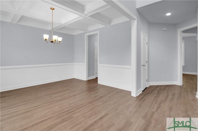 empty room with hardwood / wood-style flooring, a notable chandelier, beam ceiling, and coffered ceiling