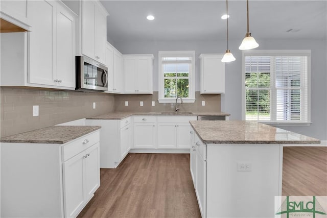 kitchen with a center island, sink, hanging light fixtures, white cabinetry, and wood-type flooring