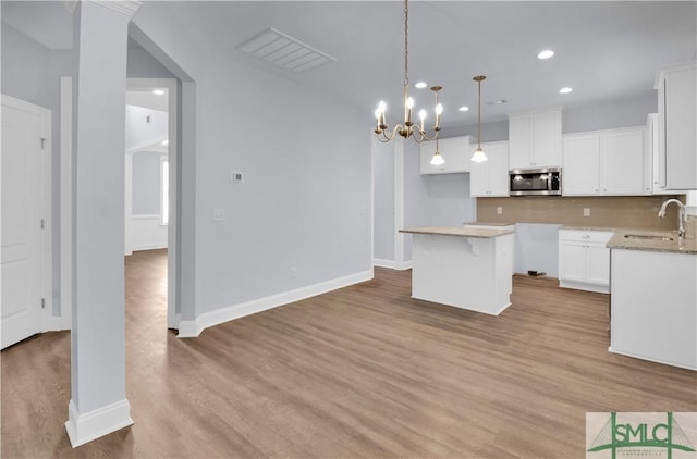 kitchen with sink, a kitchen island, decorative light fixtures, white cabinets, and light wood-type flooring