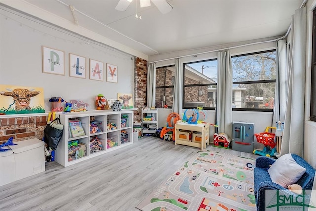 playroom with ceiling fan, light hardwood / wood-style floors, and brick wall