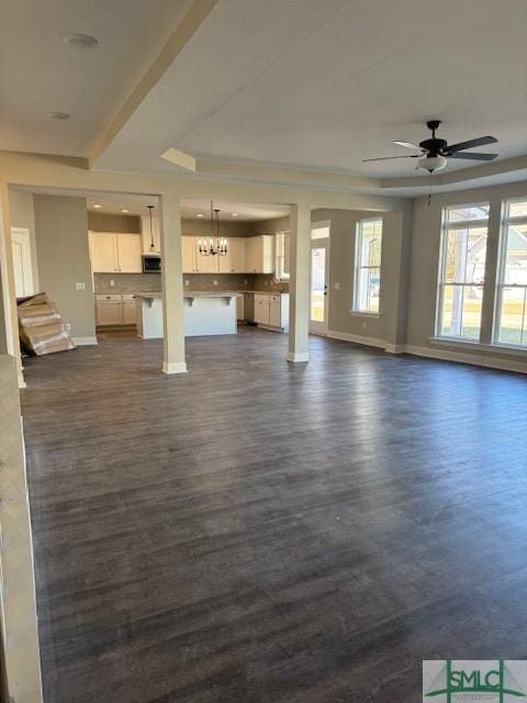 unfurnished living room featuring ceiling fan, dark hardwood / wood-style flooring, and a tray ceiling