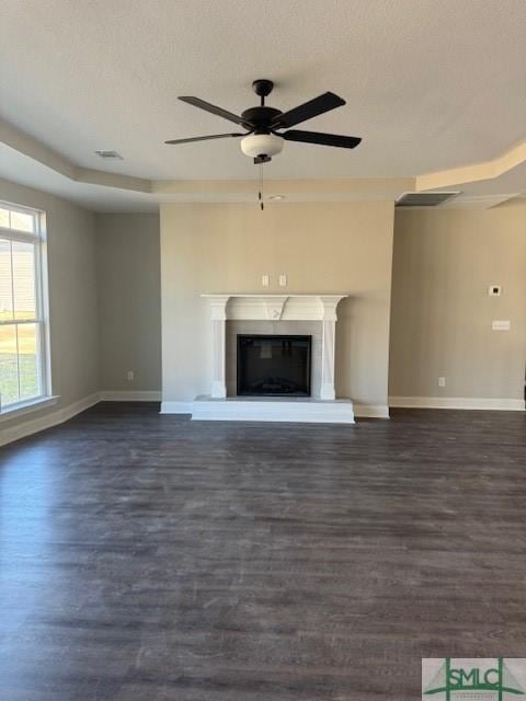 unfurnished living room featuring a raised ceiling, ceiling fan, dark hardwood / wood-style flooring, and a textured ceiling