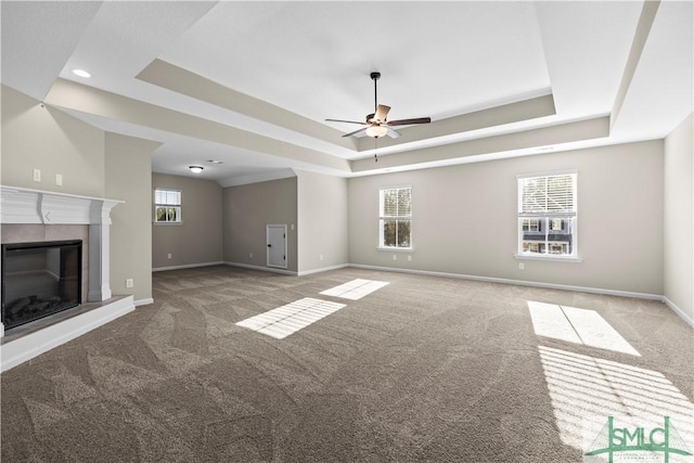 unfurnished living room with a glass covered fireplace, a raised ceiling, a wealth of natural light, and carpet floors