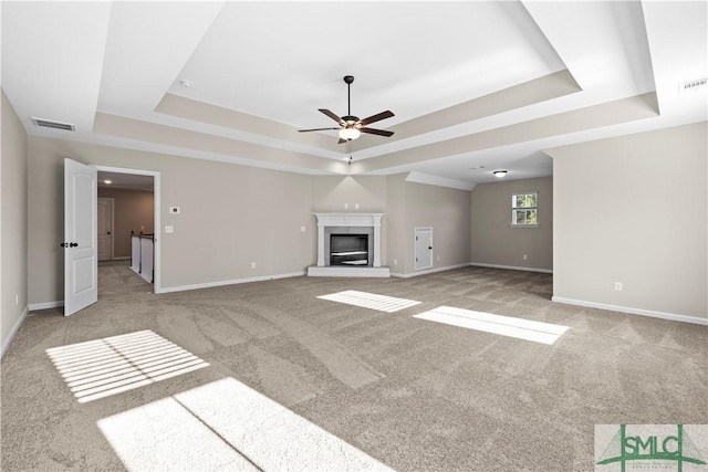 unfurnished living room featuring light carpet, a glass covered fireplace, a raised ceiling, and baseboards