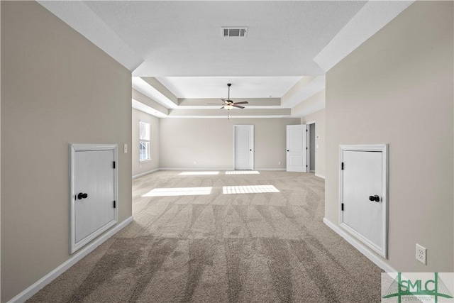 spare room with light carpet, visible vents, a raised ceiling, and baseboards