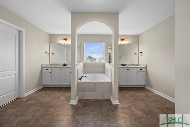 full bathroom with a sink, baseboards, two vanities, and a bath