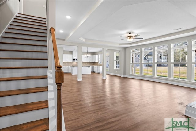 unfurnished living room featuring visible vents, ceiling fan with notable chandelier, wood finished floors, a raised ceiling, and stairs