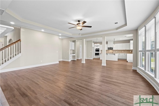 unfurnished living room with a tray ceiling, visible vents, dark wood-style flooring, and ceiling fan with notable chandelier