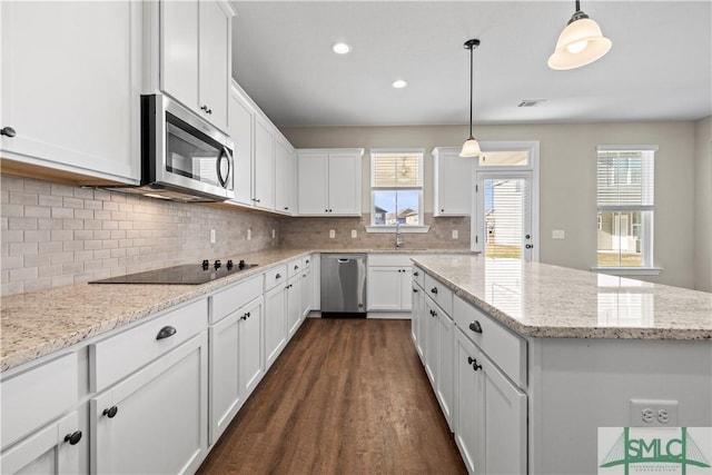 kitchen featuring visible vents, a center island, stainless steel appliances, white cabinetry, and a sink