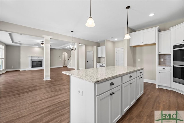 kitchen featuring a fireplace with raised hearth, a ceiling fan, white cabinetry, stainless steel double oven, and dark wood-style flooring