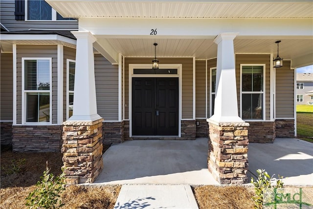 view of exterior entry with stone siding and covered porch