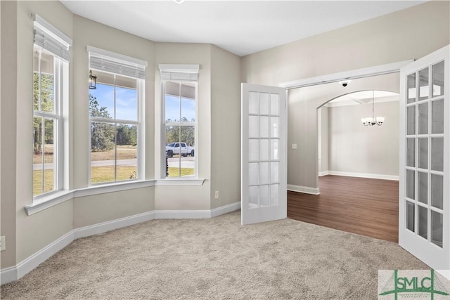 spare room featuring baseboards, carpet, french doors, arched walkways, and a notable chandelier