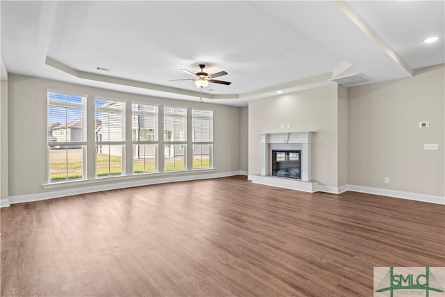 unfurnished living room featuring a glass covered fireplace, baseboards, a raised ceiling, and dark wood-type flooring