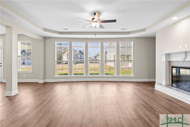 unfurnished living room featuring visible vents, wood finished floors, a glass covered fireplace, baseboards, and ceiling fan