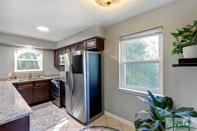 kitchen with dark brown cabinetry, stainless steel appliances, a textured ceiling, sink, and light tile patterned floors