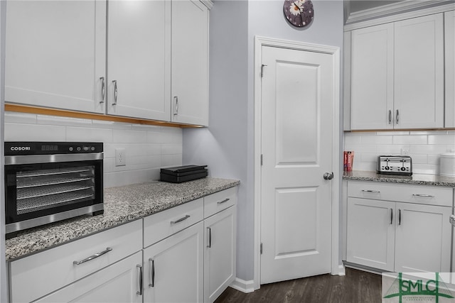 kitchen with tasteful backsplash, light stone countertops, white cabinets, and dark wood-type flooring