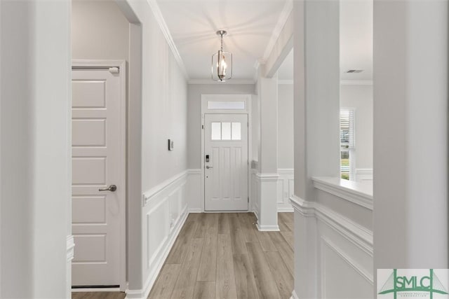 foyer featuring a wainscoted wall, light wood-style flooring, ornamental molding, an inviting chandelier, and a decorative wall