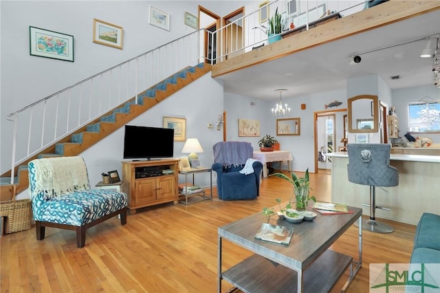 living room with a towering ceiling, an inviting chandelier, and light hardwood / wood-style flooring