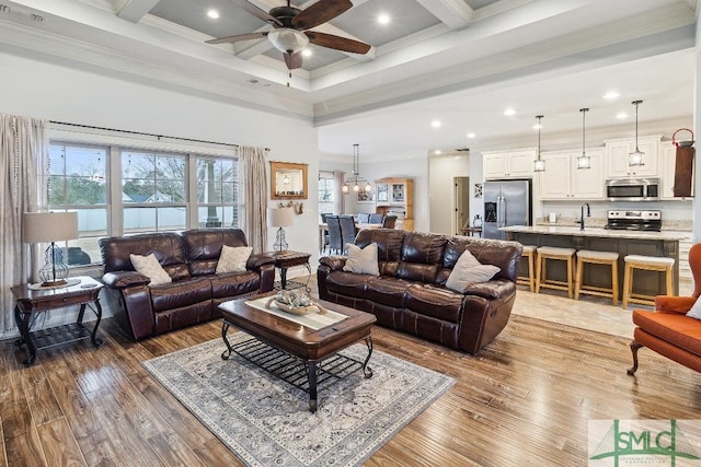 living room with hardwood / wood-style floors, beamed ceiling, ornamental molding, ceiling fan with notable chandelier, and sink