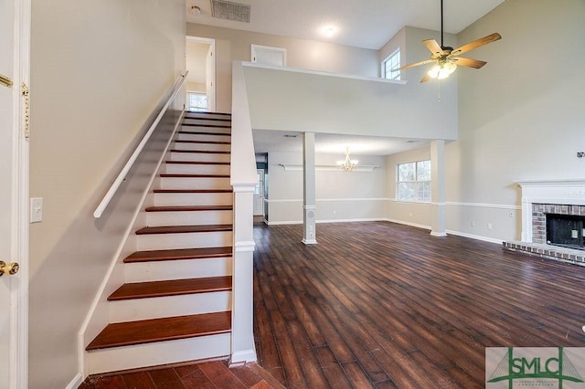 stairway with ceiling fan with notable chandelier, a towering ceiling, a fireplace, and hardwood / wood-style flooring