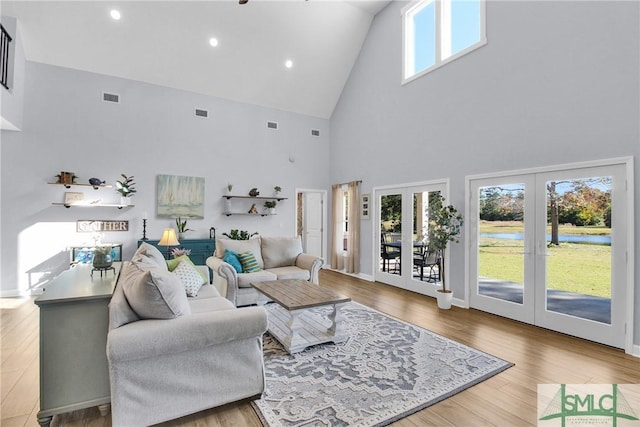 living room with light hardwood / wood-style floors, a towering ceiling, and french doors