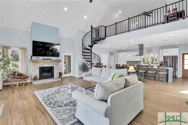 living room featuring a healthy amount of sunlight, a stone fireplace, high vaulted ceiling, and light hardwood / wood-style flooring