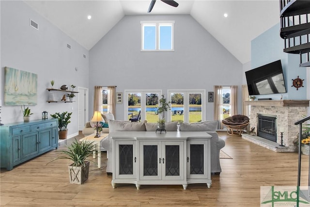 living room with ceiling fan, a stone fireplace, plenty of natural light, and high vaulted ceiling