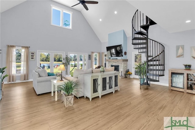 living room with french doors, light wood-type flooring, ceiling fan, a fireplace, and a high ceiling