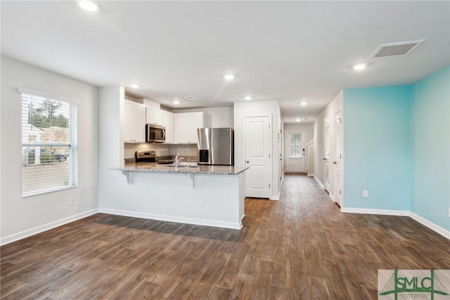 kitchen featuring appliances with stainless steel finishes, kitchen peninsula, light stone counters, dark hardwood / wood-style floors, and white cabinets