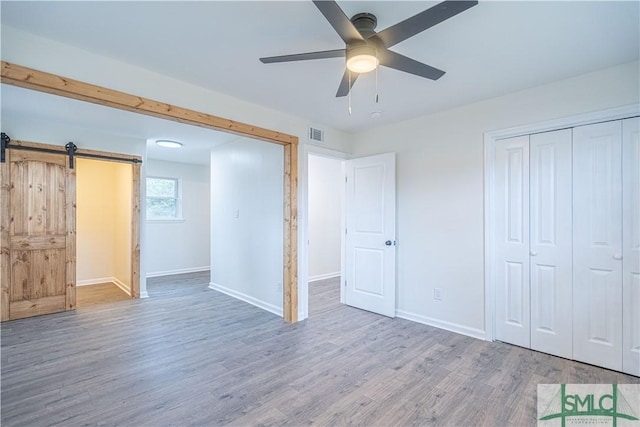 unfurnished bedroom featuring ceiling fan, hardwood / wood-style floors, a closet, and a barn door