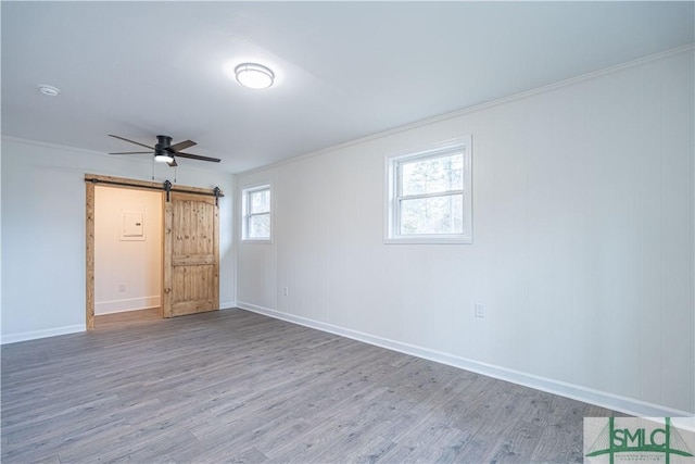 unfurnished bedroom with ceiling fan, ornamental molding, a barn door, and wood-type flooring