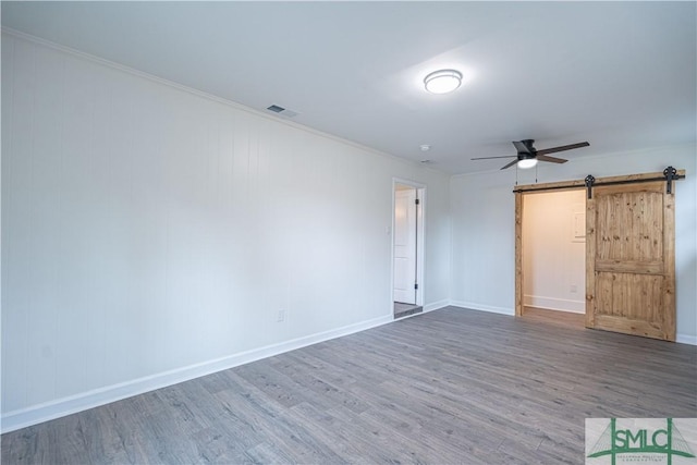 unfurnished bedroom with ornamental molding, wood-type flooring, ceiling fan, and a barn door