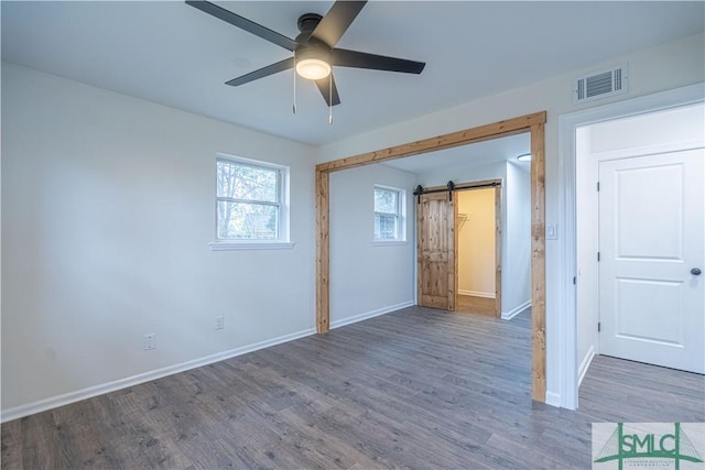 unfurnished room with dark wood-type flooring, ceiling fan, and a barn door