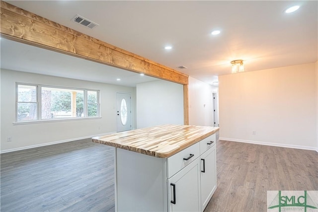 kitchen featuring white cabinets, wood-type flooring, butcher block countertops, a kitchen island, and beam ceiling