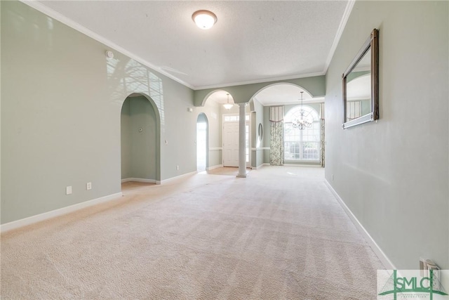 carpeted spare room with ornamental molding, a notable chandelier, decorative columns, and a textured ceiling