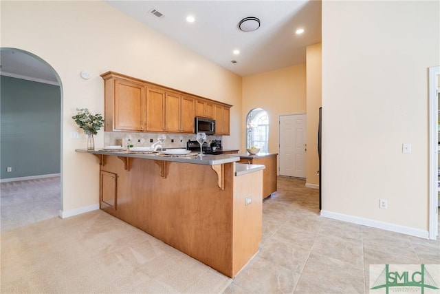 kitchen featuring black electric range, a kitchen breakfast bar, kitchen peninsula, a high ceiling, and light colored carpet