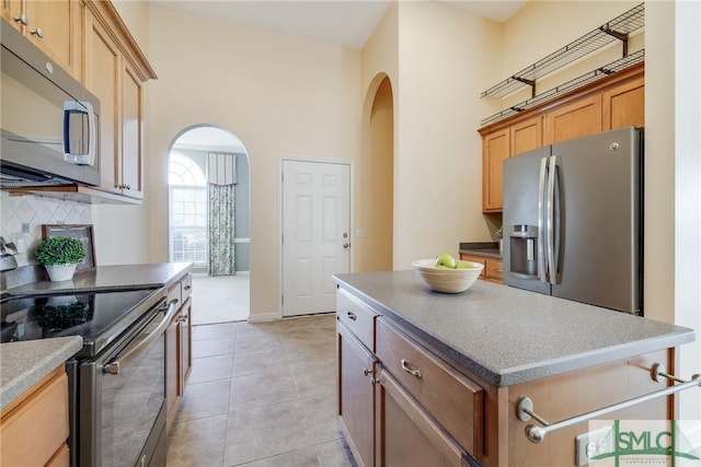 kitchen with stainless steel appliances, a center island, light tile patterned floors, decorative backsplash, and a high ceiling