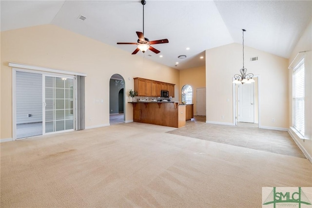 unfurnished living room with high vaulted ceiling, light carpet, a wealth of natural light, and ceiling fan with notable chandelier