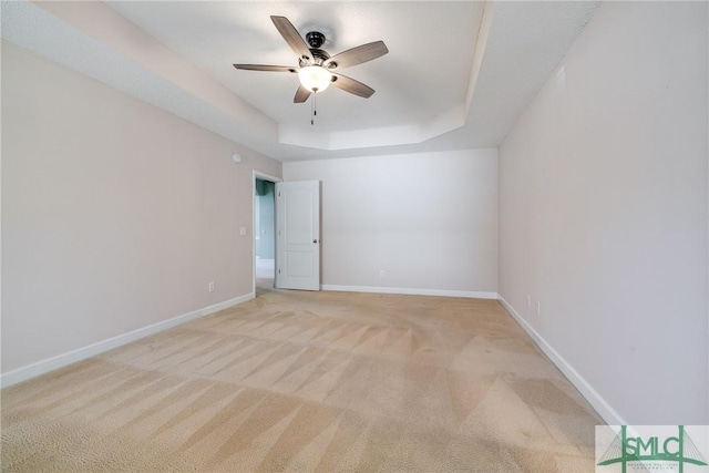 empty room featuring ceiling fan, light colored carpet, and a raised ceiling