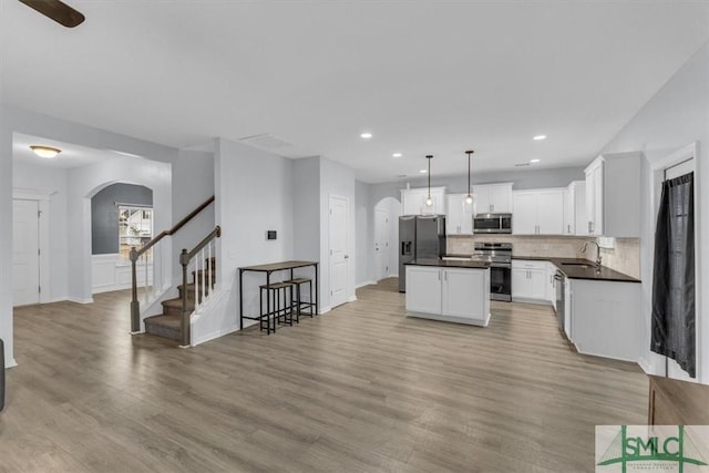 kitchen with pendant lighting, stainless steel appliances, a kitchen island, white cabinets, and sink