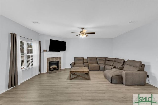 living room featuring a tiled fireplace, ceiling fan, and light hardwood / wood-style flooring