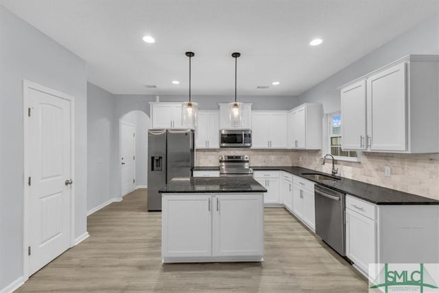 kitchen with appliances with stainless steel finishes, hanging light fixtures, a kitchen island, sink, and white cabinetry