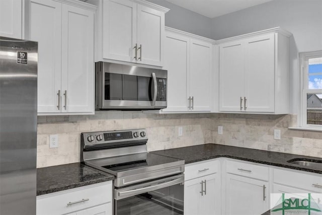 kitchen with stainless steel appliances, white cabinetry, dark stone countertops, and tasteful backsplash