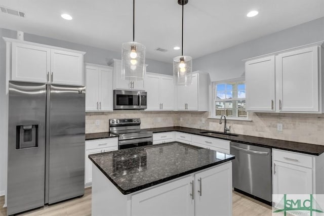 kitchen featuring appliances with stainless steel finishes, a center island, sink, white cabinetry, and decorative light fixtures